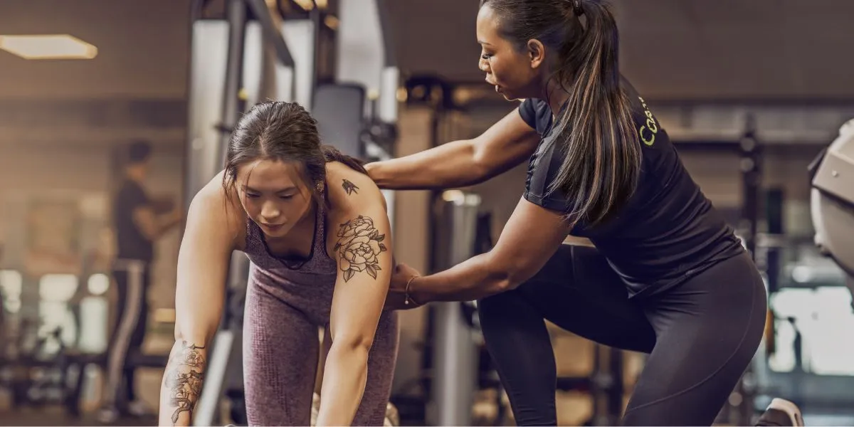 Personal trainer correcting a woman's form during a gym workout