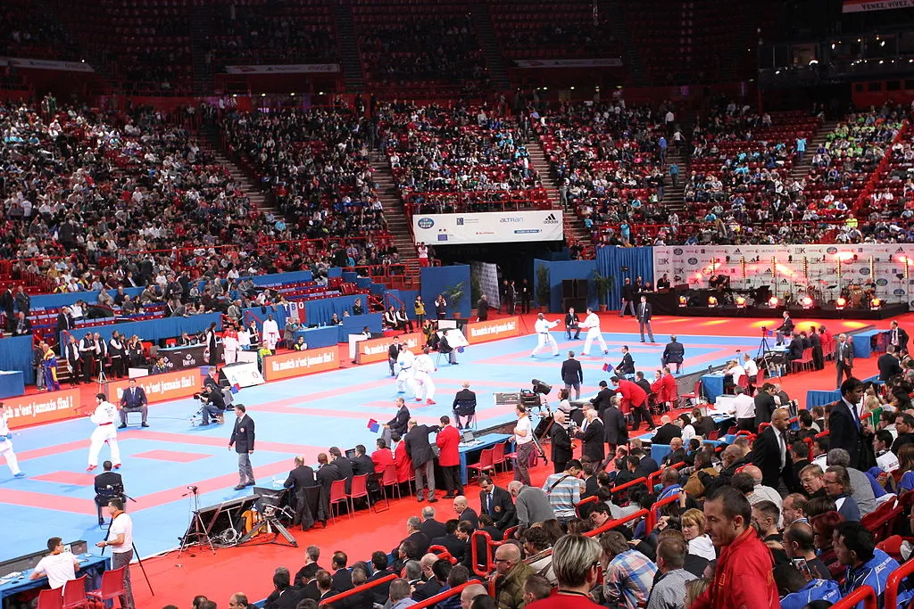 Karate tournament under way on multiple mats in a large arena full of spectators