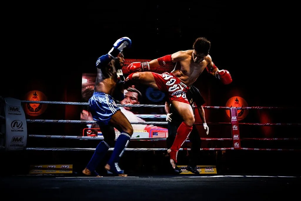 Two Muay Thai fighters exchanging kicks in a ring under dramatic lighting