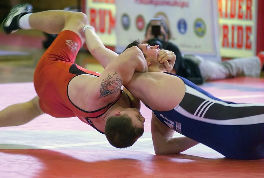 Two wrestlers in singlets grappling on the mat, one bridging to avoid a pin