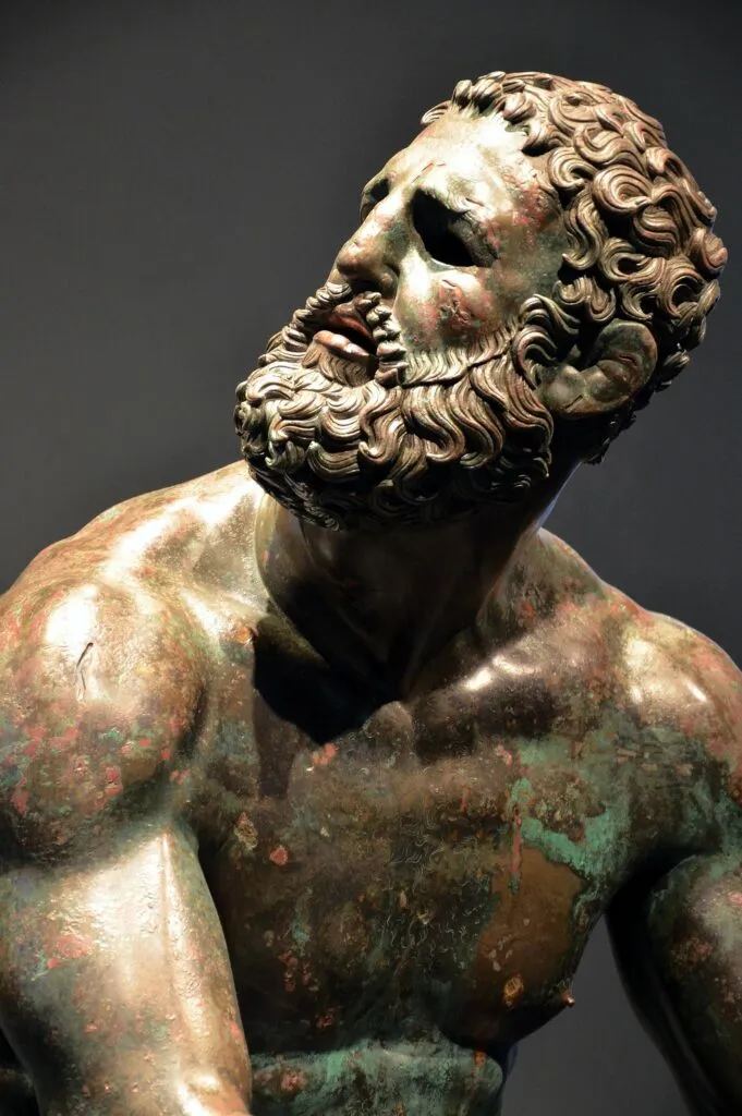 Ancient bronze statue of a seated boxer with a battered face and swollen ears