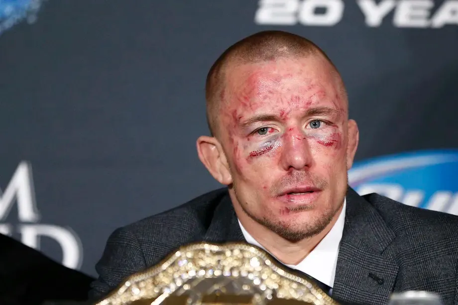 MMA fighter with a cut and bruised face seated at a press conference with a championship belt