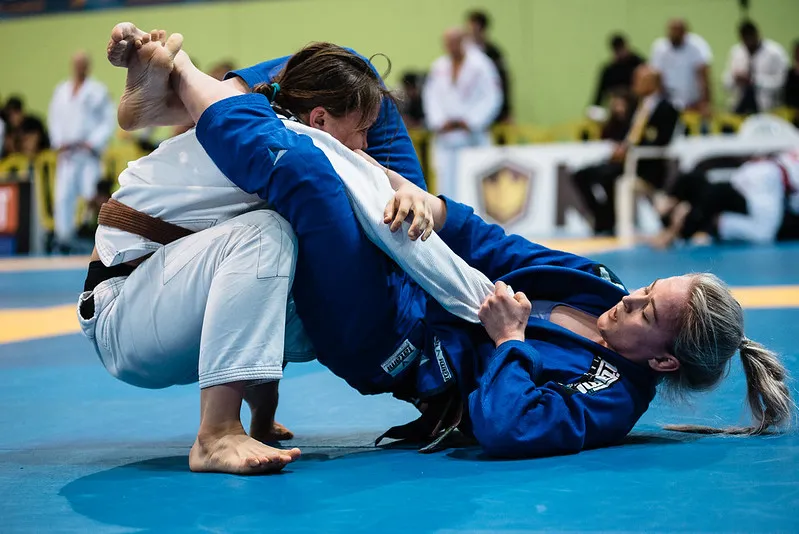 Two Brazilian jiu-jitsu competitors grappling on a blue mat at a tournament