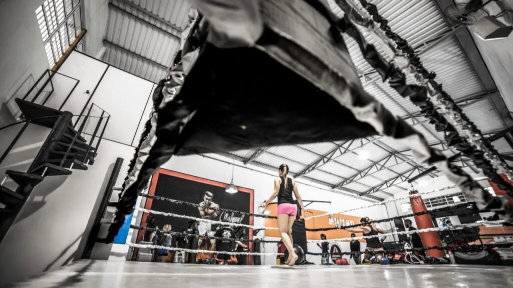 Wide view of a boxing gym with a woman skipping beside the ring