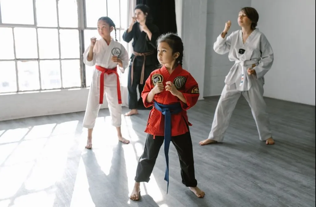 Girl in a red uniform in a fighting stance with other students and an instructor behind her