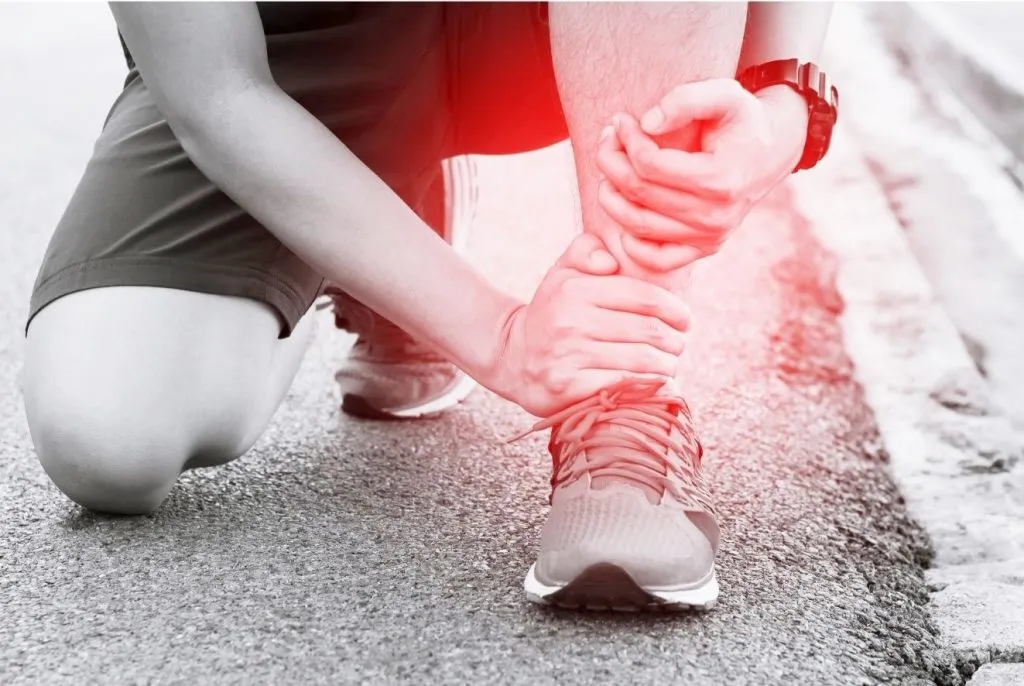 Runner crouched on the road gripping a painful ankle highlighted in red