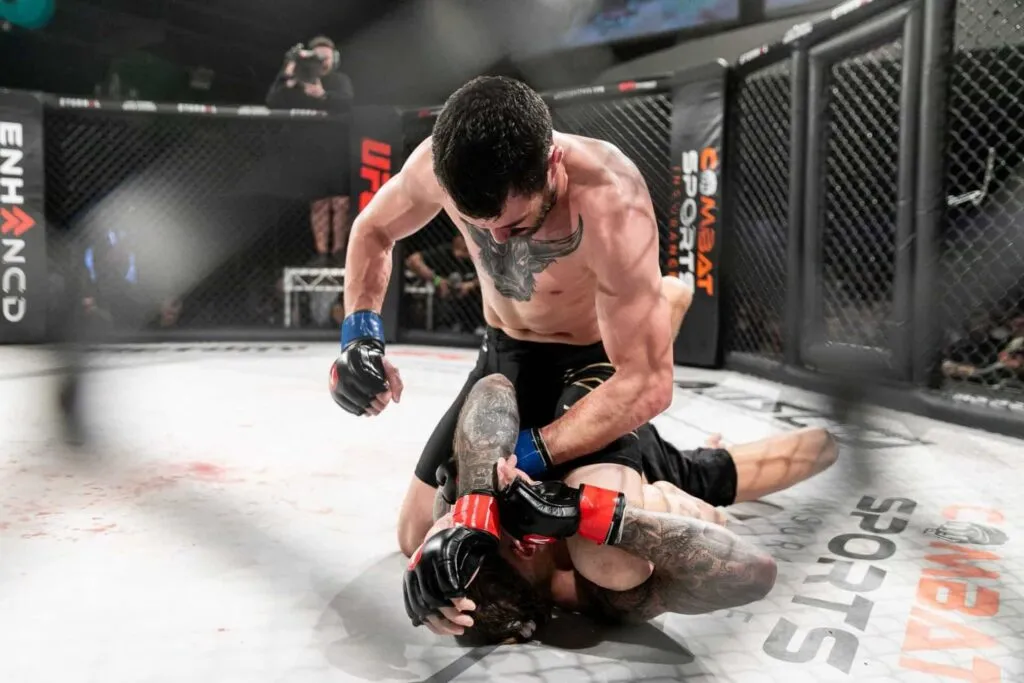 MMA fighter in top position throwing punches at a downed opponent in the cage