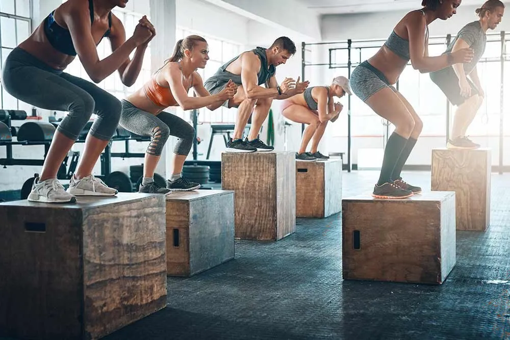 Group fitness class doing box jumps together in a gym