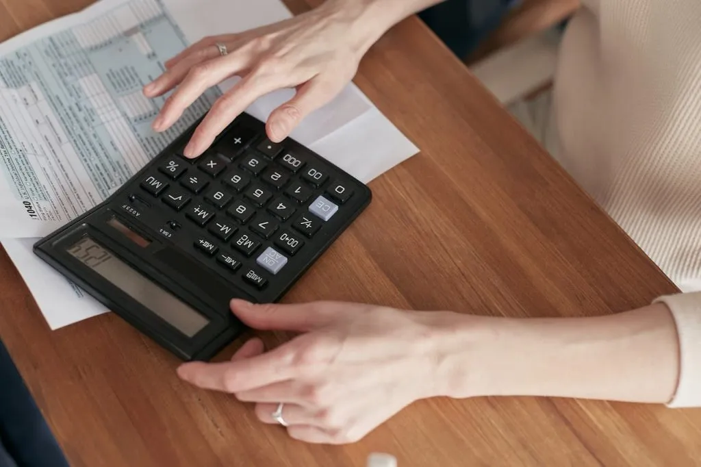 Hands using a calculator on a desk covered in paperwork