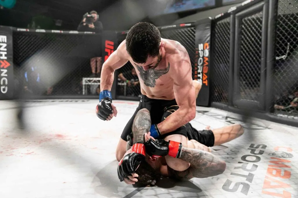 MMA fighter in top position throwing punches at a downed opponent in the cage
