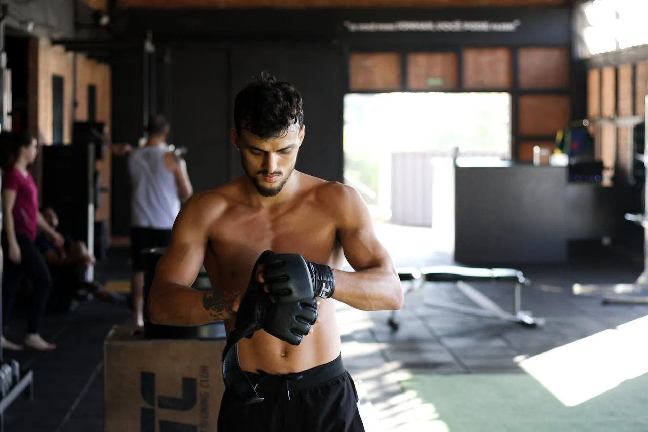 Shirtless fighter in MMA gloves standing in a gym before training
