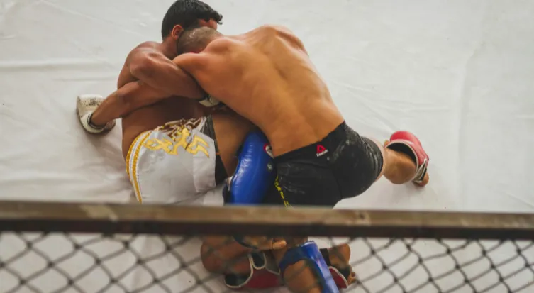 Two Muay Thai fighters clinching in the ring, seen through the ropes