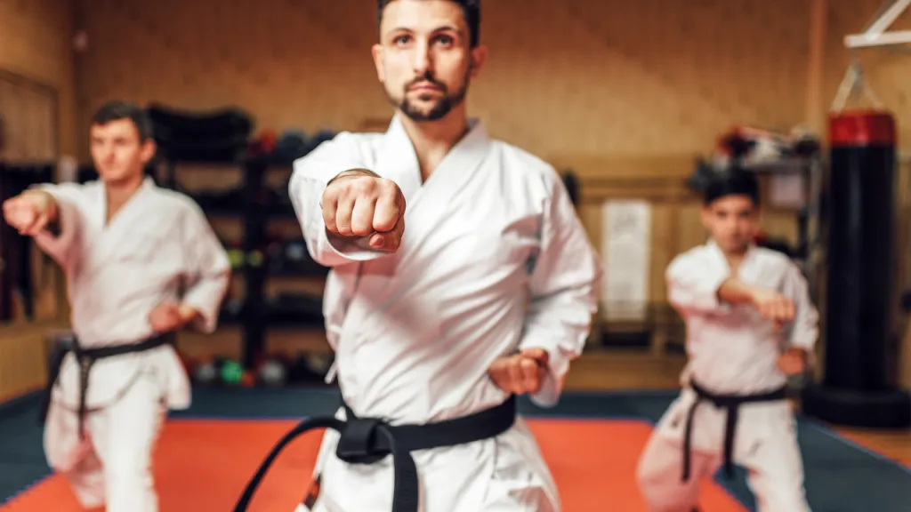 Karate instructor in a white gi punching towards camera with students training behind him