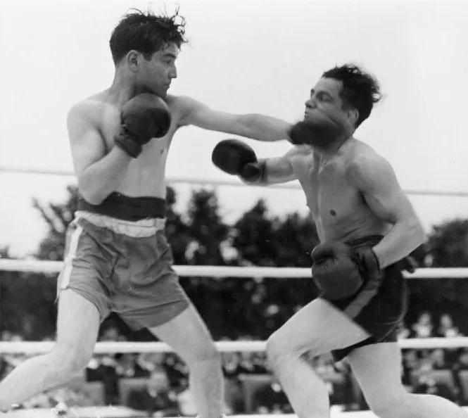 Black and white historical photo of two boxers trading punches in an outdoor ring