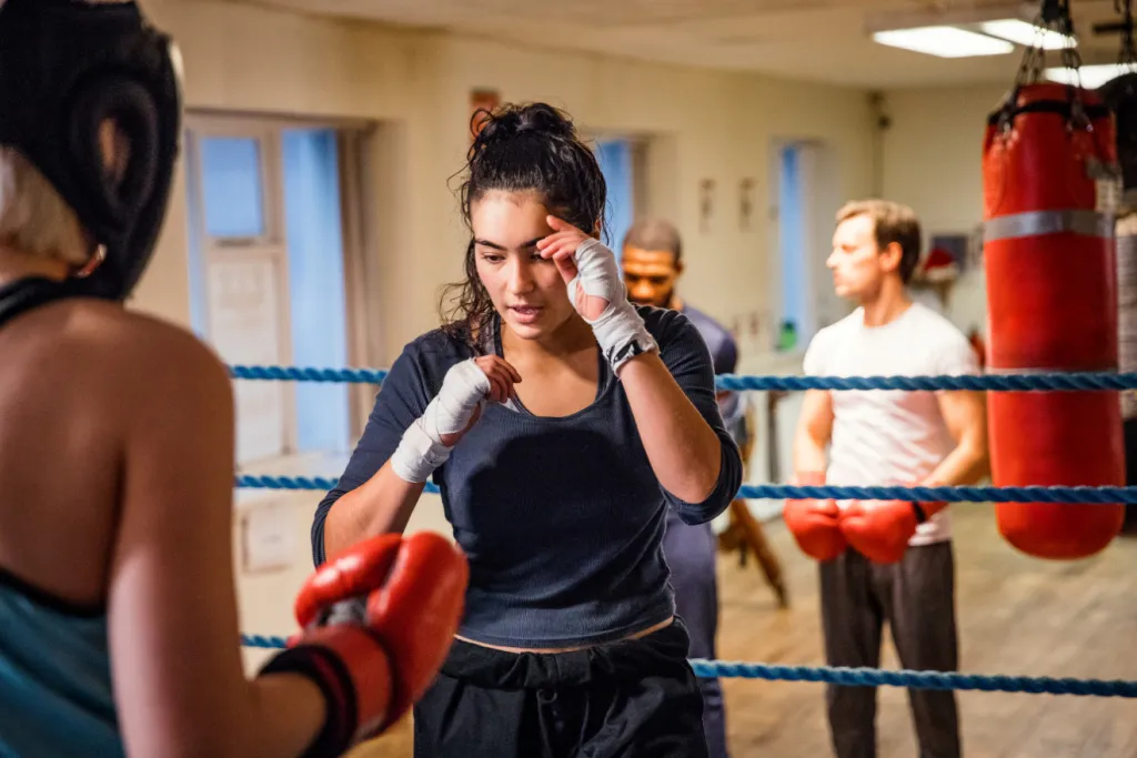 Female boxer in red gloves and hand wraps training in a ring while others watch