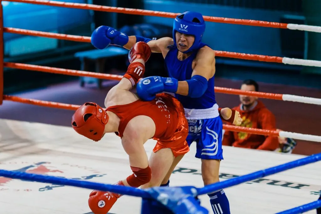 Amateur boxer in red headgear doubled over from a body shot during a ring bout