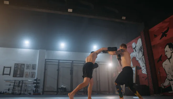 Two kickboxers sparring in a gym with a red mural on the wall behind them
