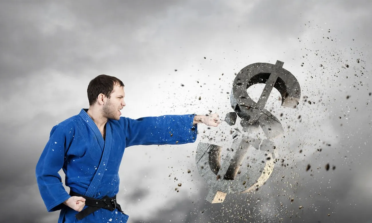 Man in a blue judo gi punching through a stone dollar sign