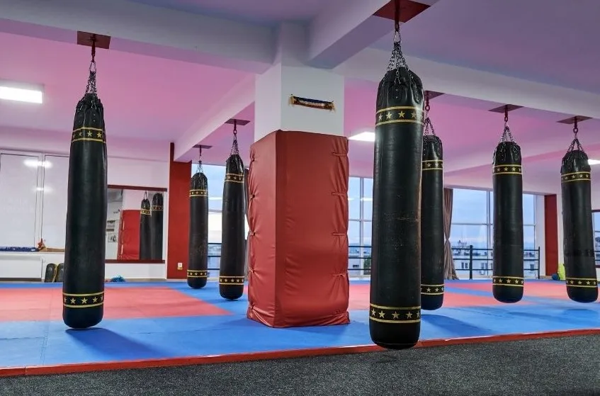 Kickboxing gym with heavy bags hanging over a red and blue mat