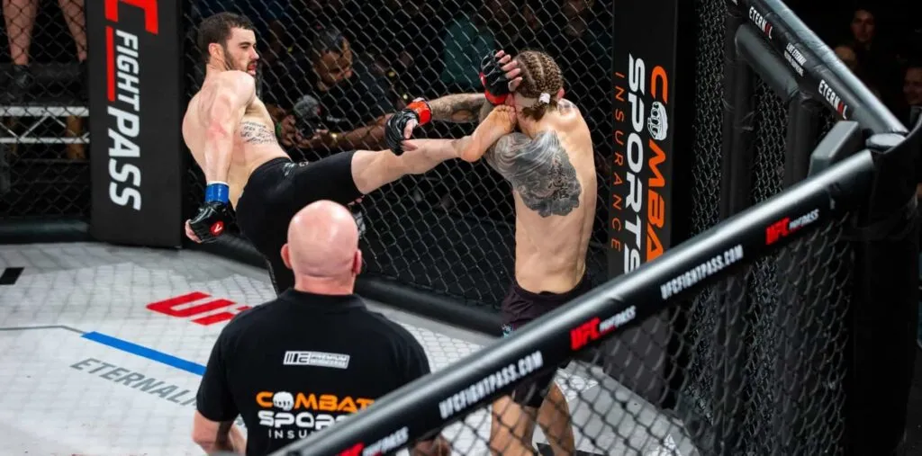 MMA fighter landing a head kick beside a Combat Sports Insurance cage banner while officials watch