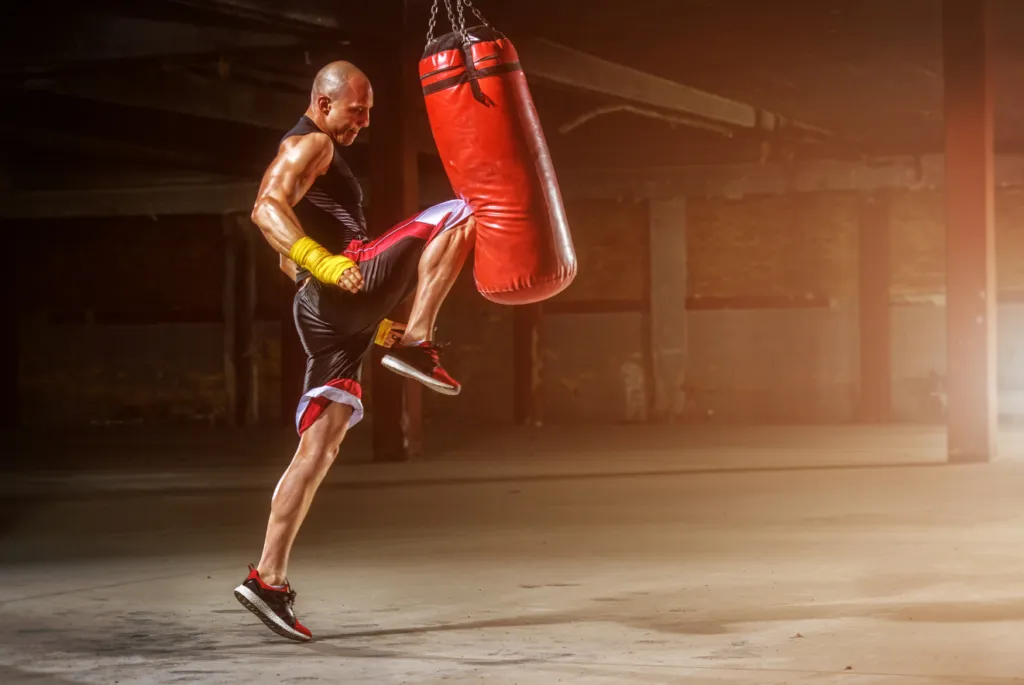 Kickboxer in yellow hand wraps driving a knee into a red heavy bag