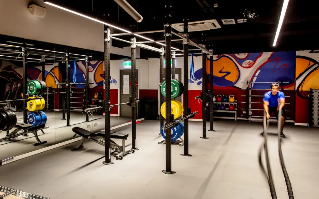 Man swinging battle ropes in a modern strength gym with squat racks and a graffiti wall