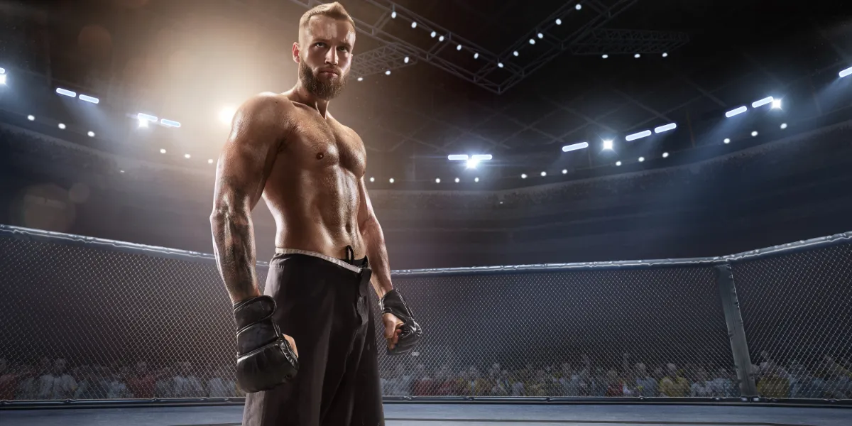 Shirtless fighter in gloves standing in an arena cage under stadium lights