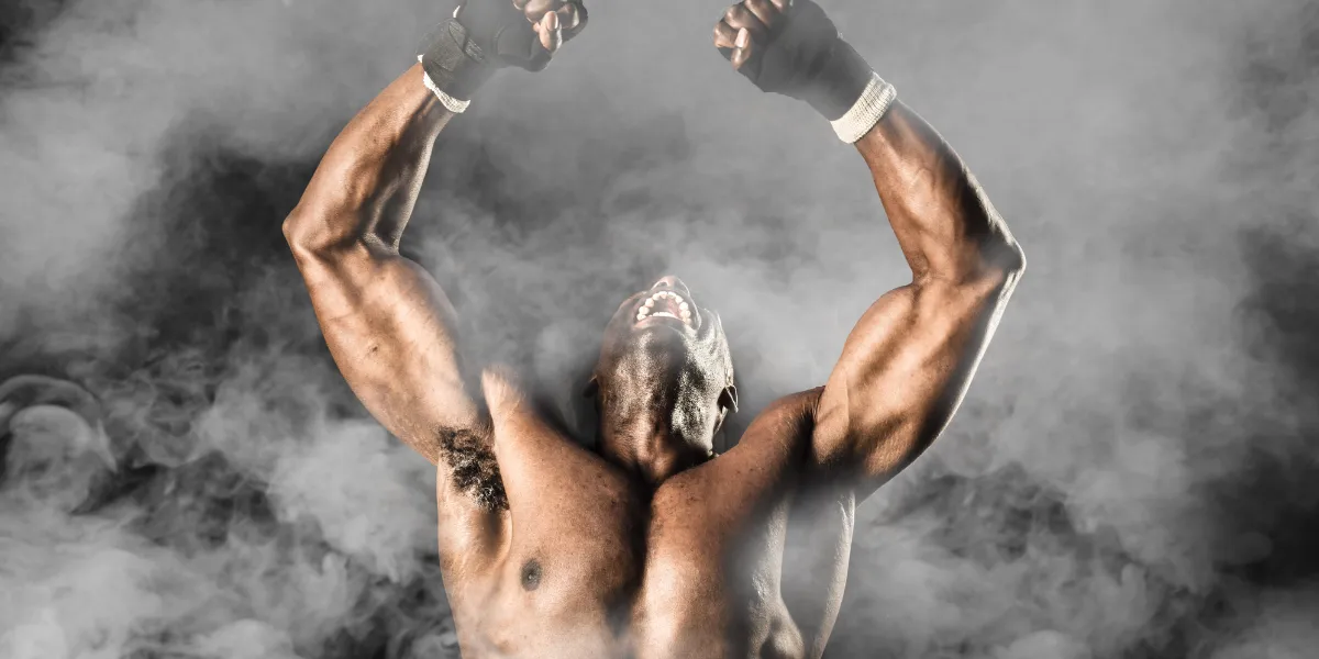 Muscular fighter raising both fists in a cloud of smoke