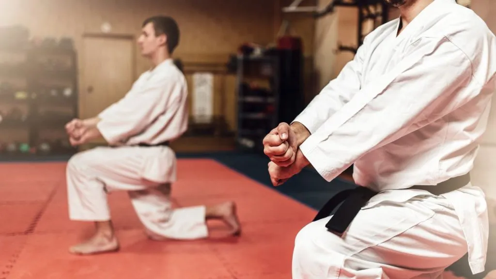 Two karate students in white gis kneeling in a dojo
