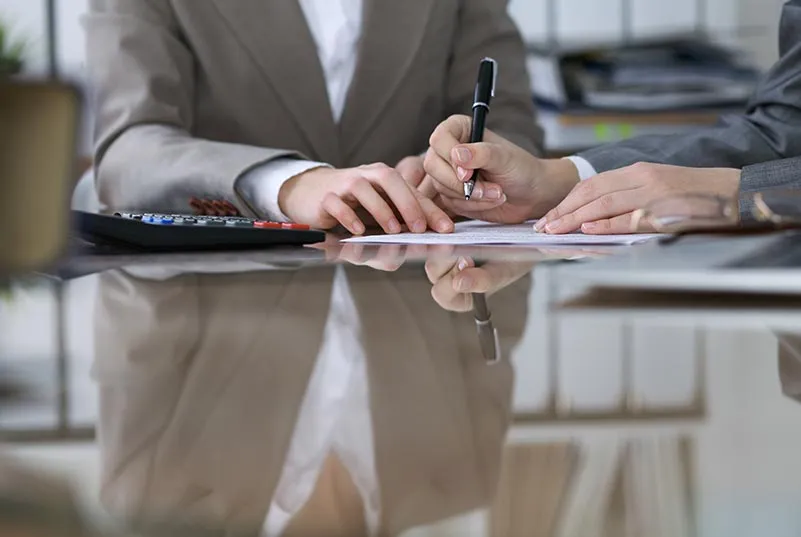 Person in a suit writing on paperwork next to a calculator