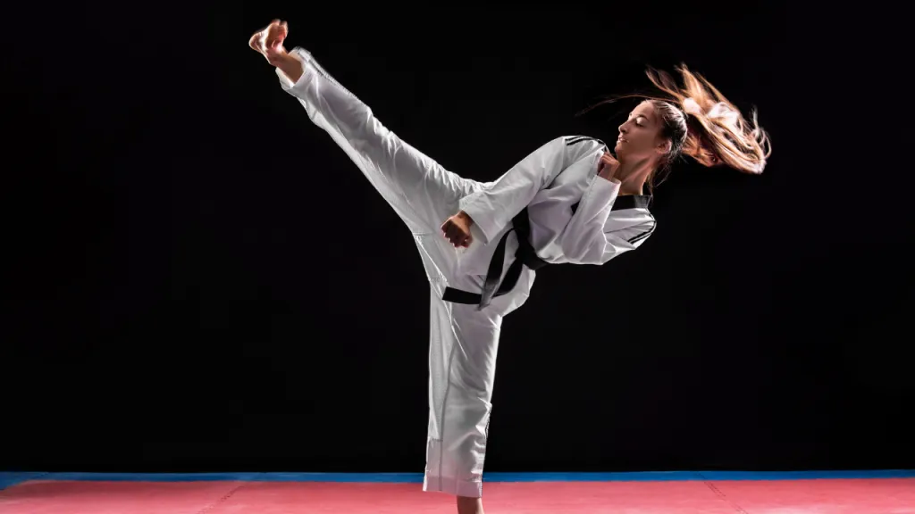 Taekwondo athlete in a white dobok throwing a high kick against a black background