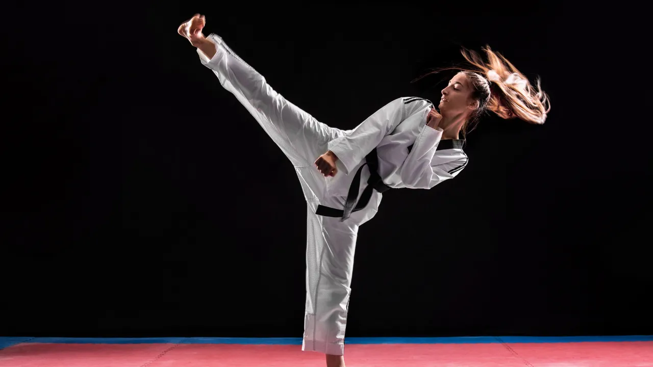 Taekwondo athlete in a white dobok throwing a high kick against a black background