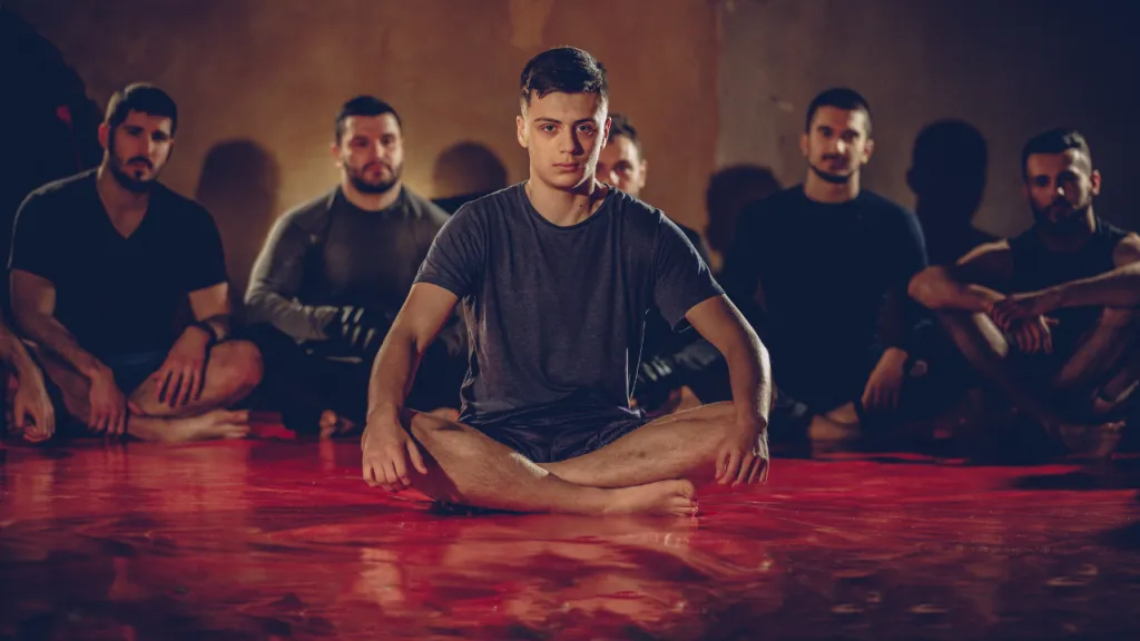 Fighter sitting cross-legged on a red mat with teammates seated behind him