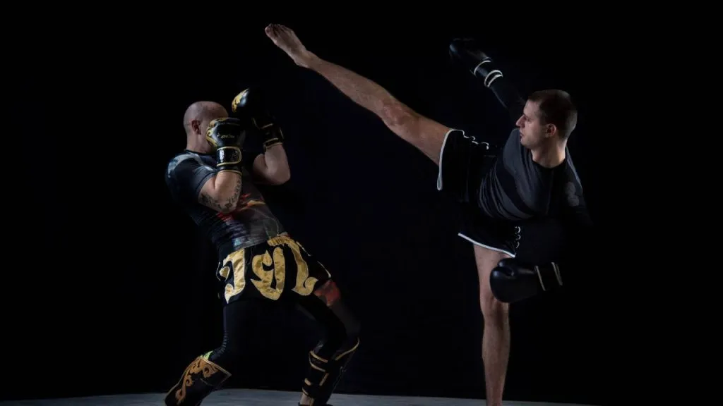 Kickboxer landing a high kick on an opponent's guard against a black background