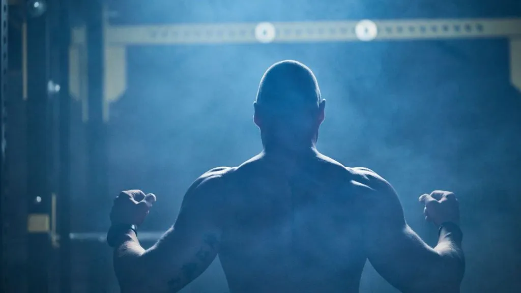 Silhouette of a muscular fighter flexing under blue gym lights