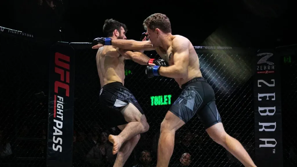 Two MMA fighters exchanging punches against the cage at a professional event
