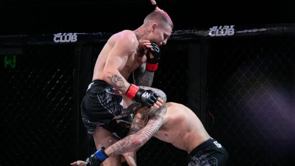 Two MMA fighters clinching against the cage fence