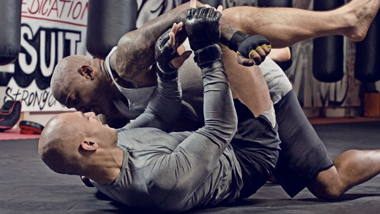 Two grapplers training on the mat, one working from guard in a gym