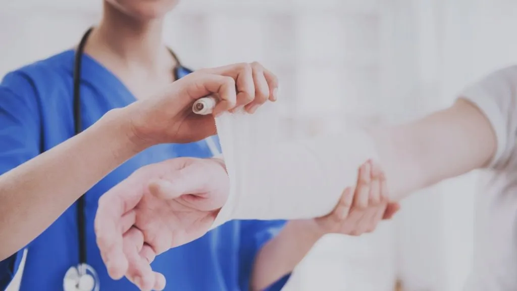 Nurse in blue scrubs bandaging a patient's wrist