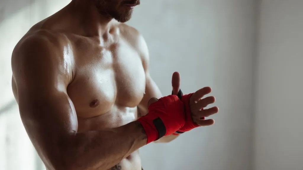 Shirtless boxer wrapping his hands in red hand wraps