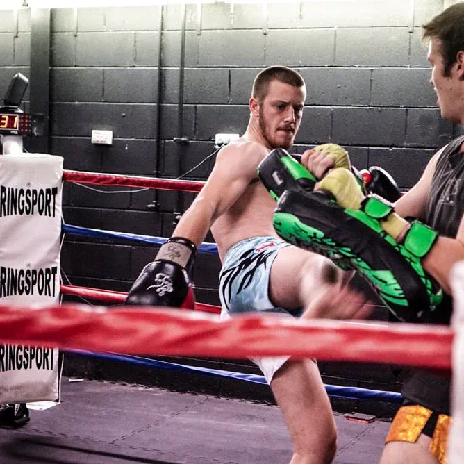 Muay Thai fighter kicking green pads held by a coach in a ring