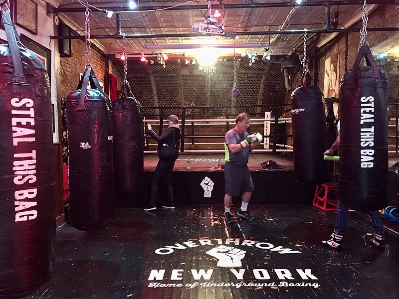 Underground boxing gym with heavy bags hanging around a central ring