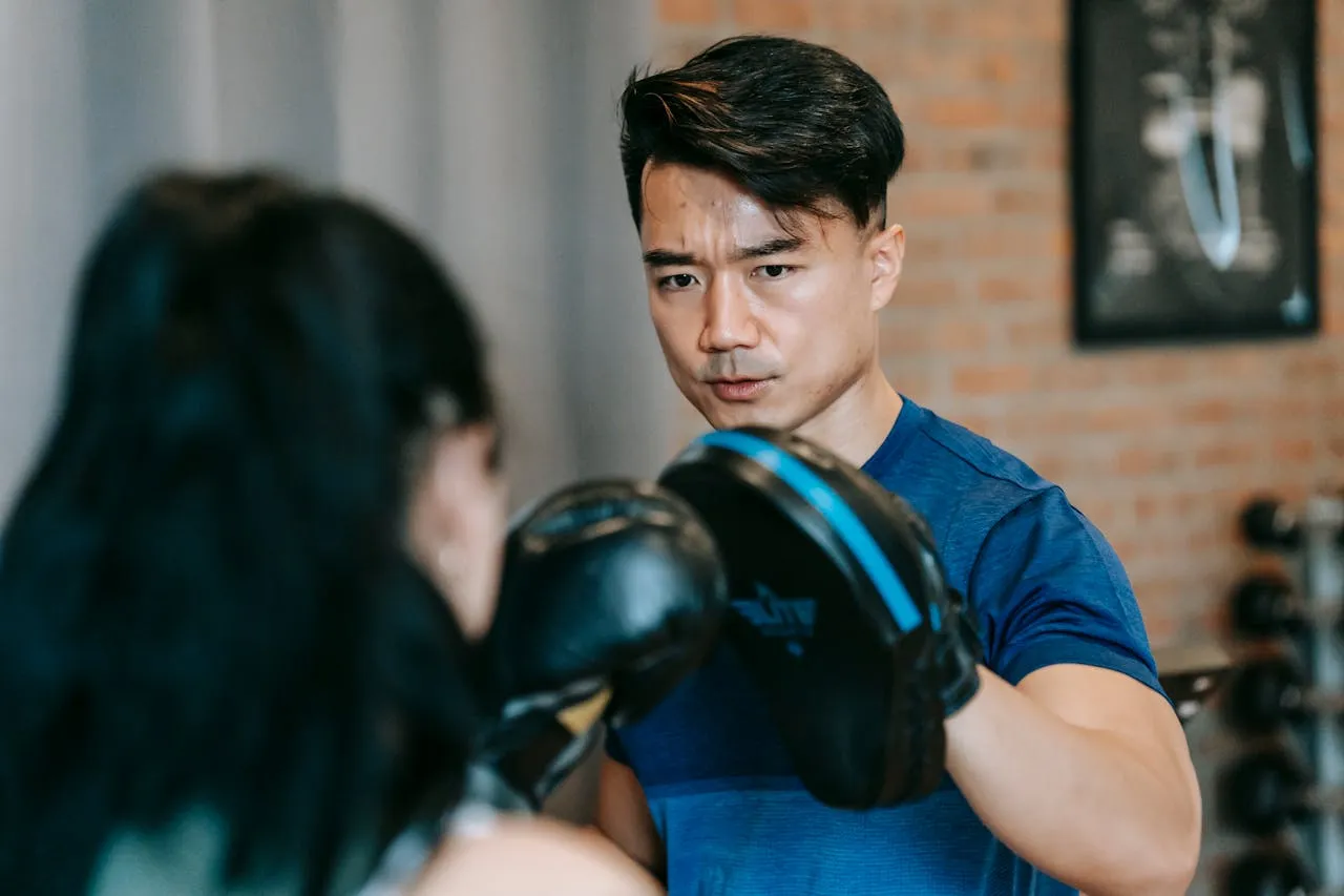 Coach holding focus mitts for a woman in boxing gloves in a gym