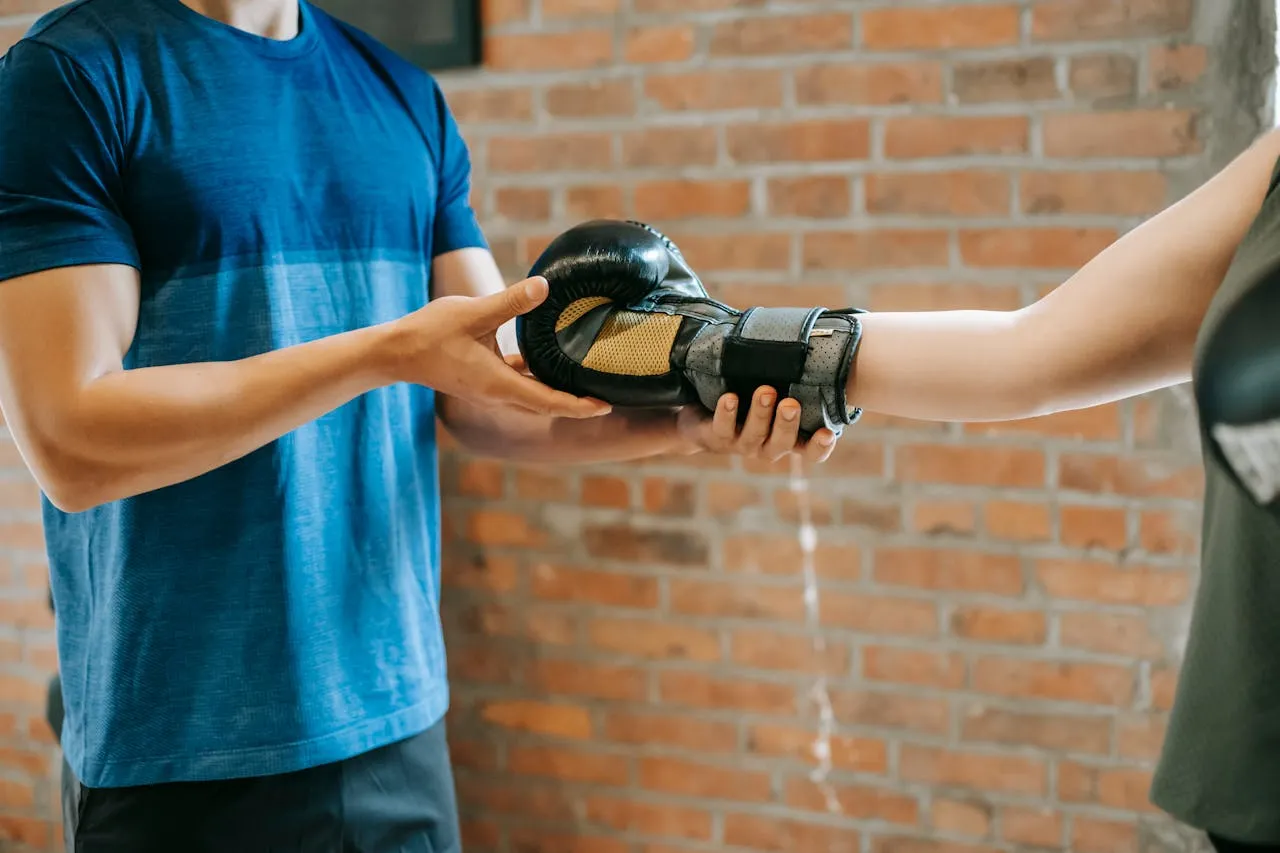 Coach helping a boxer put on a glove in front of a brick wall