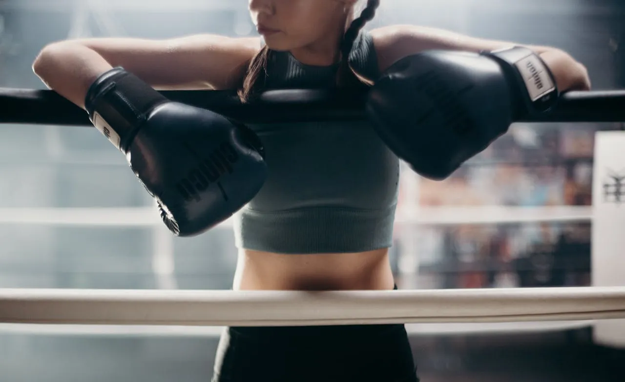 Boxer in gloves resting her arms on the ropes of a ring