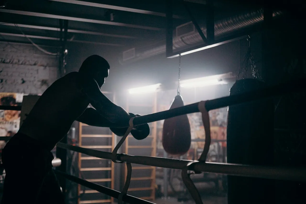 Silhouette of a boxer leaning on the ropes in a dim gym