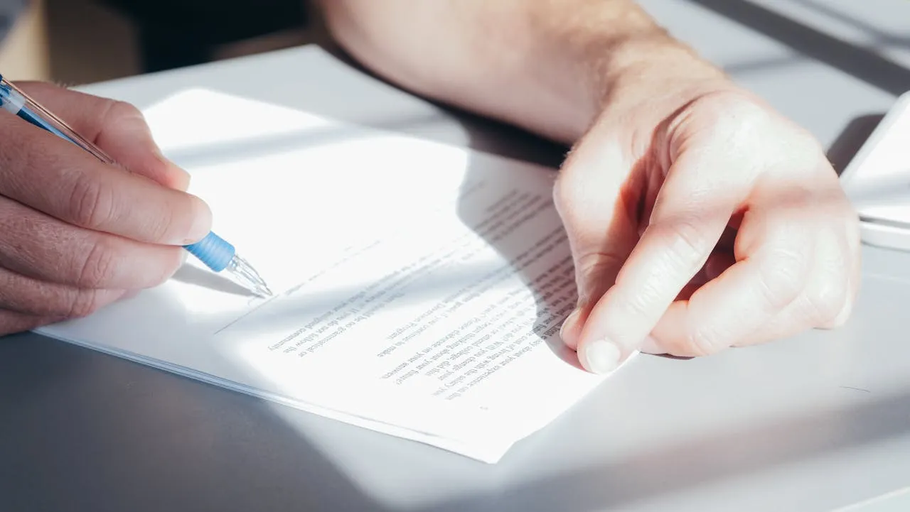 Close-up of a hand signing a document with a blue pen