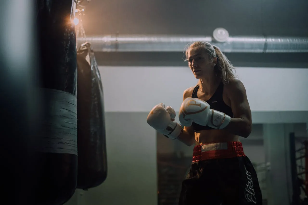 Female boxer in gloves standing between heavy bags in a dark gym