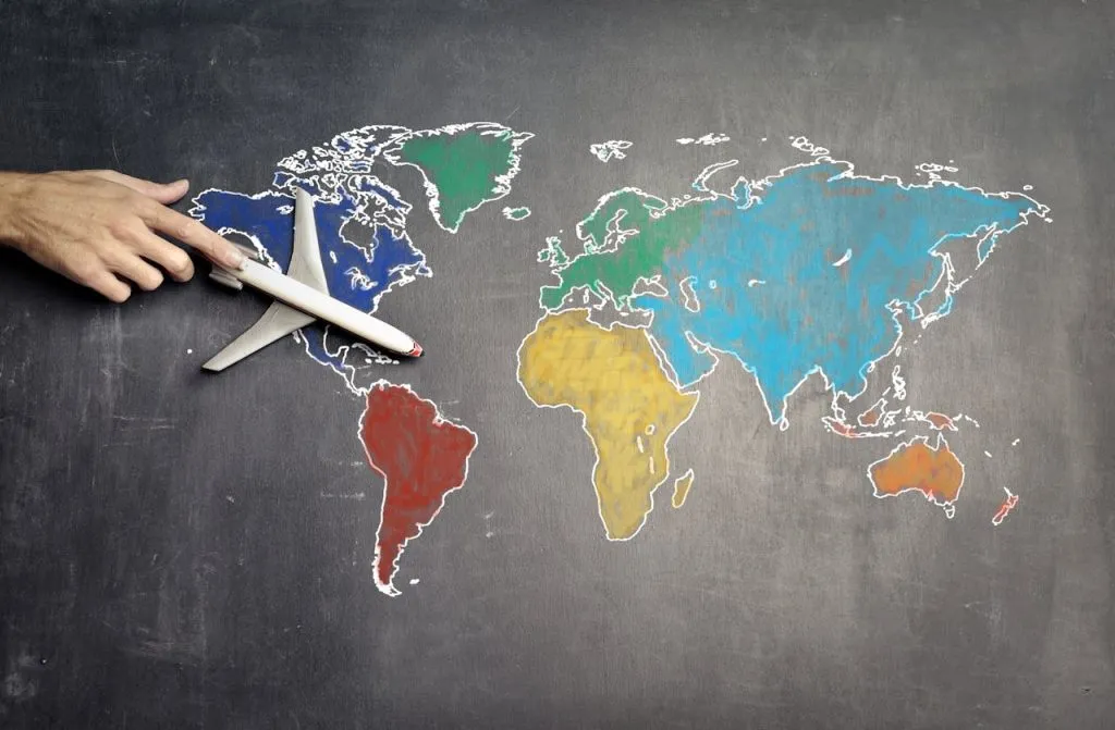 Hand holding a toy plane over a chalk-drawn map of the world
