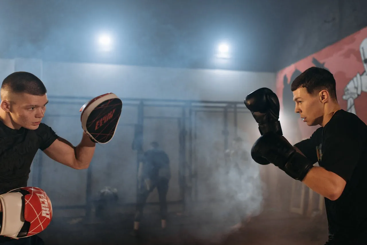 Coach holding focus mitts for a boxer in a smoky gym